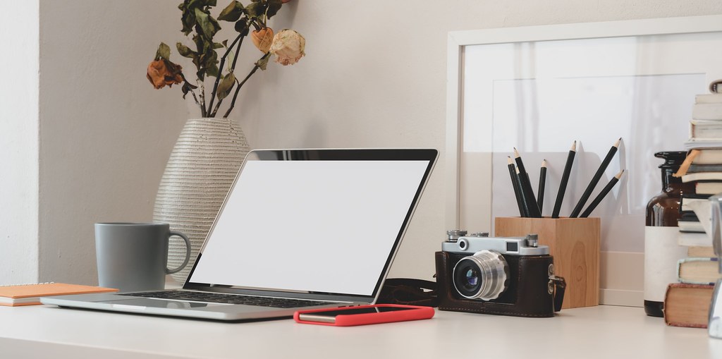 A clean, professional workspace featuring a laptop and notebook on a wooden desk in a bright office.